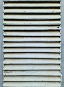 Weathered white louvered ventilation panel with peeling paint