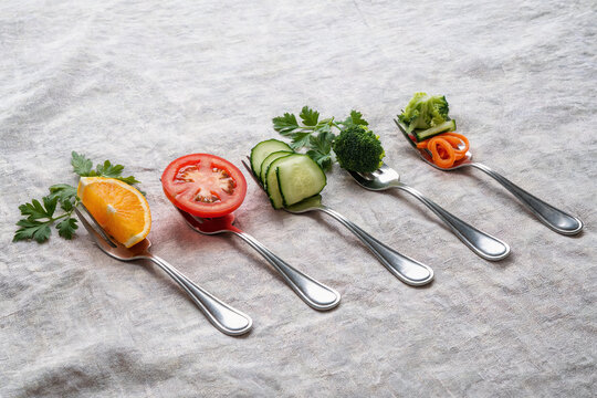 Healthy fresh vegetable and fruit pieces on forks arranged in a row on fabric background