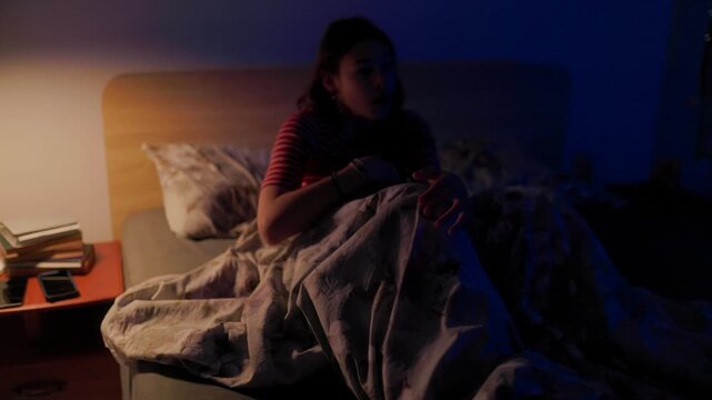 Terrified young girl waking up from nightmare gasping for air in dark bed