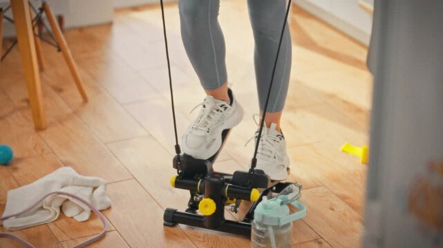 A girl in white sneakers and leggings follows a trainer's cues, stepping on a home stepper for a cardio session in daylight, showcasing convenient indoor exercise as a gym-free alternative