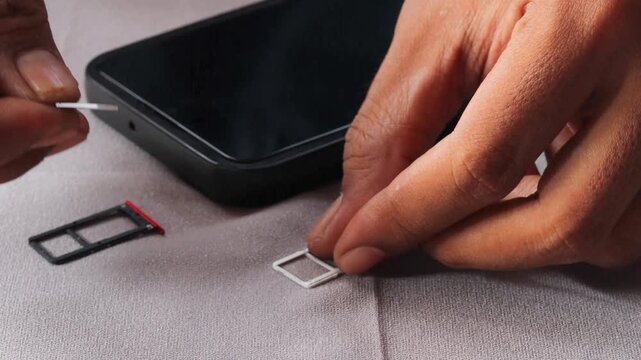 Close-up view of an Asian  man's hands carefully swapping sim card inside smartphone, sitting at table with grey surface with extraction tray nearby during mobile service transition.