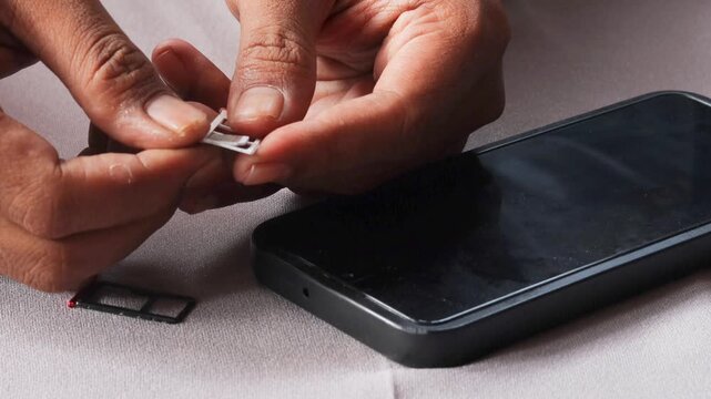 Close-up view of an Asian  man's hands carefully swapping sim card inside smartphone, sitting at table with grey surface with extraction tray nearby during mobile service transition.