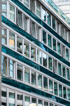 Rows of green glass windows repeat across a building facade, where urban architecture uses grid rhythm and exterior repetition to shape a precise pattern