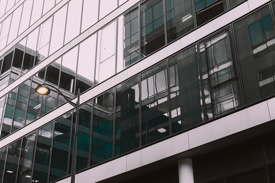 An angle in urban architecture looks across a glass building facade, where windows, reflection and a column define the exterior depth
