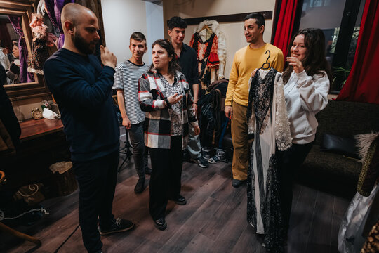 Young actors in a theatre dressing room examine costumes and talk about wardrobe. A small group of performers prepares backstage and rehearses for an upcoming show.