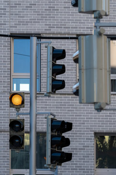 Traffic light poles stand before a brick building facade, where amber signal, windows and urban street equipment form a layered city view