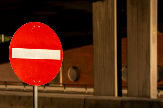 Red no entry sign stands inside a shaded parking structure, where circular traffic symbol, barrier color and concrete background define restriction
