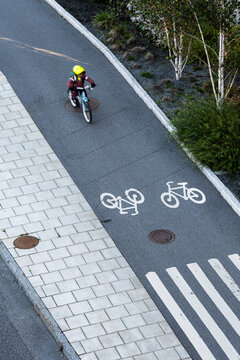 Small cyclist rides along a bicycle lane from above, where road markings, crossing stripes, traffic signs and urban pavement shape the route