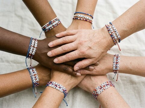 Diverse group of people stacking hands wearing USA 250 patriotic beaded bracelets. Unity and community celebration concept for Independence Day. Symbol of national pride and togetherness.