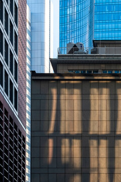 Tall glass towers frame a shadowed concrete facade, where windows, reflection, urban architecture and wall lines compress vertical city depth