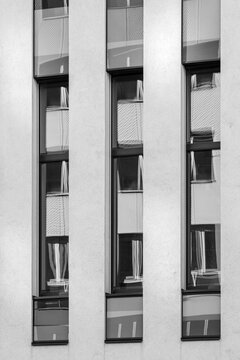 A vertical concrete facade with narrow windows forms a monochrome urban architecture pattern, where wall rhythm, shadow and building detail align