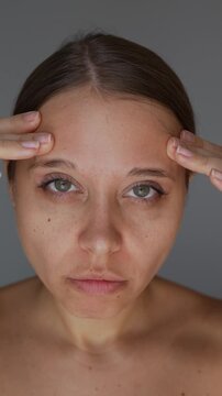 Young woman touching her forehead and showing active facial expression with visible forehead wrinkles. Dissatisfied reaction to expression lines and aging skin concept