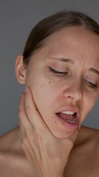 Young woman holding her jaw and moving it with painful expression. Jaw pain, facial tension, TMJ disorder, toothache, muscle spasm and discomfort concept