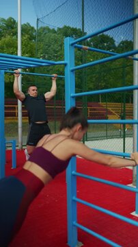 Athletic people perform an outdoor sport workout. A man does pull-ups while a woman stretches for fitness.