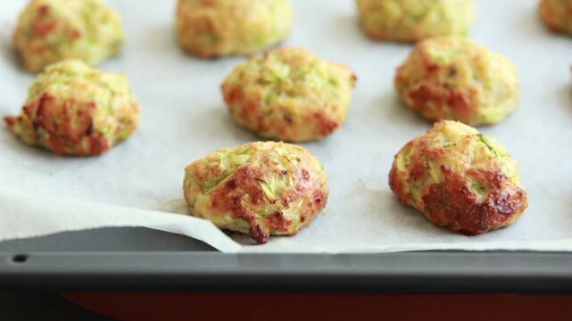 Close-up of golden, crispy baked zucchini tots freshly cooked and resting on a baking sheet lined with parchment paper