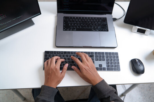 Top View of Developer Working on Laptop with Code on Screen and Keyboard Input