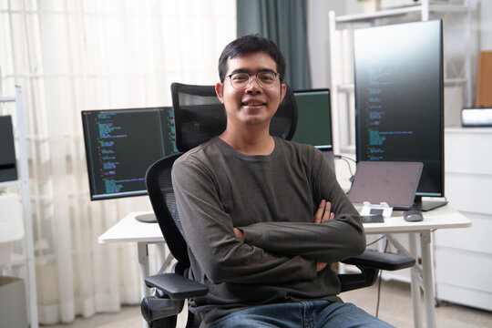 Young Developer Sitting in Front of Dual Monitors Displaying Code for Software Development