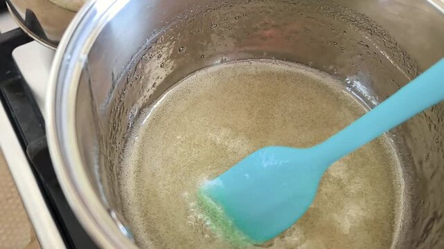 Stirring boiling sugar syrup with agar agar in pot with blue silicone spatula