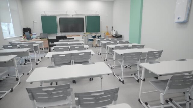 Modern classroom displays neat rows of white double desks paired with grey plastic chairs. Musical instruments placed near teaching area