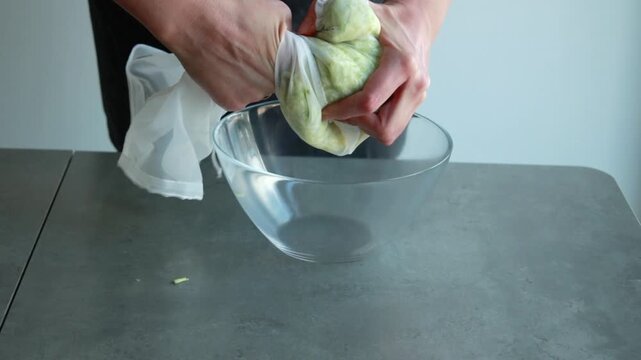 Close-up of a woman's hands squeezing and draining liquid from grated zucchini inside a mesh bag