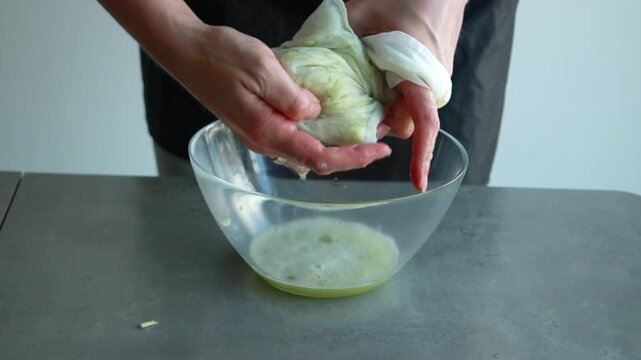Close-up of a woman's hands squeezing and draining liquid from grated zucchini inside a mesh bag