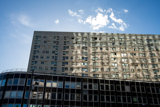 Apartment buildings in Paris catch sunlight under blue sky, where residential windows, facade shadows and urban architecture define a broad exterior view