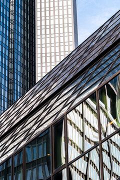 A diagonal glass facade in Frankfurt Bankenviertel, Germany, catches reflection from nearby office towers, where urban architecture forms sharp depth