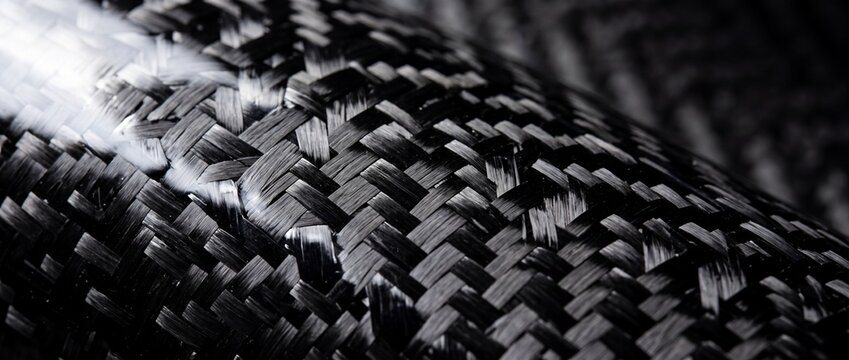 Close up texture of woven black carbon fiber material showing intricate interlaced threads and shiny reflective surface