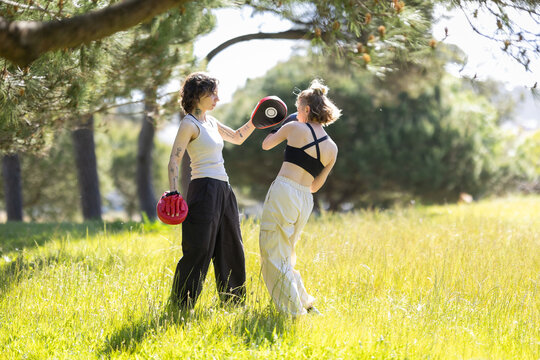 Women training boxing with focus mitts outdoors