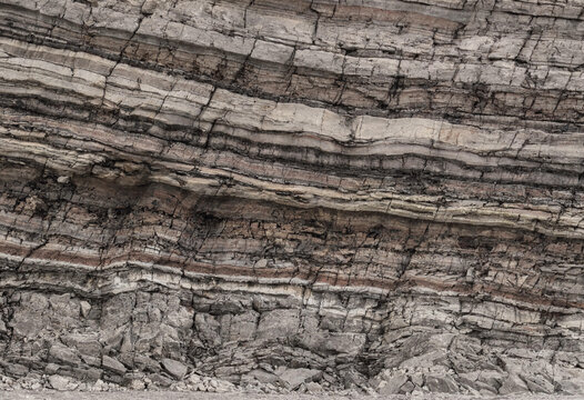 Close up of layered sedimentary rock face showing distinct horizontal strata with varying shades of brown grey and white mineral deposits