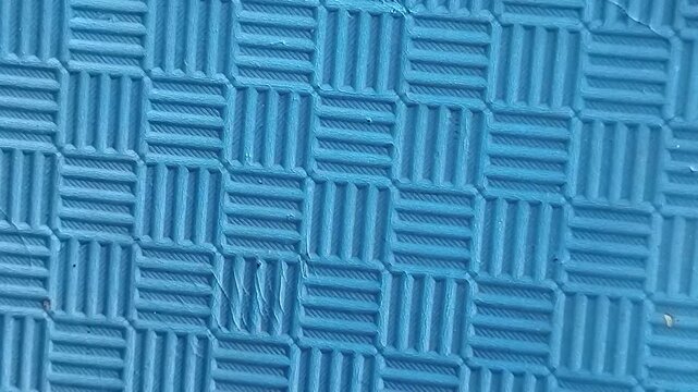 Close-up shot of a textured blue rubber mat with a grid pattern. Abstract background with geometric lines and non-slip surface texture, ideal for industrial, flooring, or design concepts.