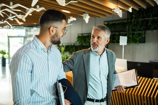 Senior manager mentoring junior colleague in modern office lobby