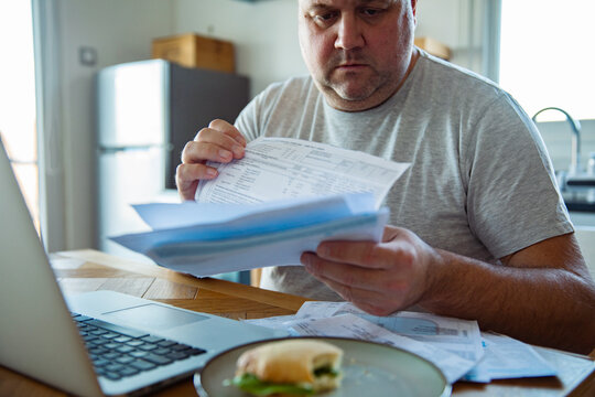 Man reviewing household bills at kitchen table with laptop
