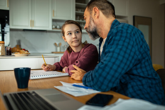 Father helping teenage daughter with homework at kitchen table