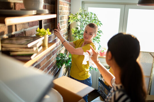 Two women hanging picture while unpacking at home