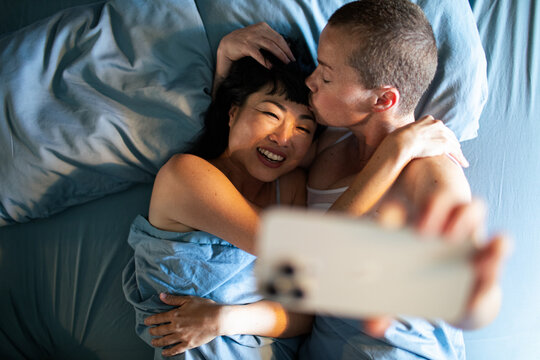 Happy couple cuddling in bed taking selfie at home