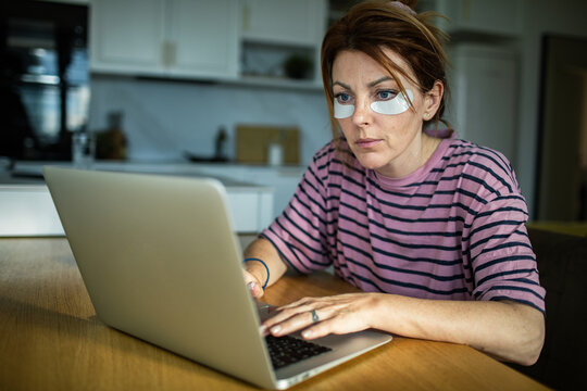 Woman working on laptop at home with under-eye patches