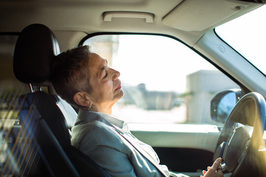 Senior woman resting in driver's seat of parked car