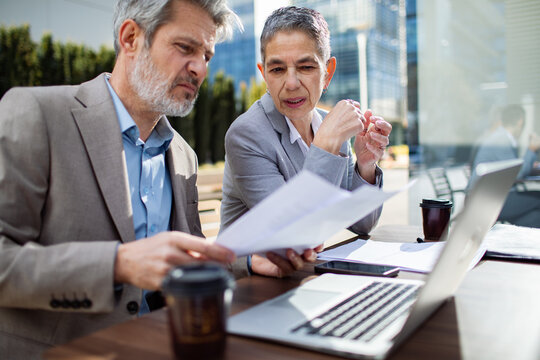 Two senior business colleagues reviewing documents at an outdoor cafe