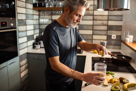 Middle-aged man making healthy smoothie in home kitchen