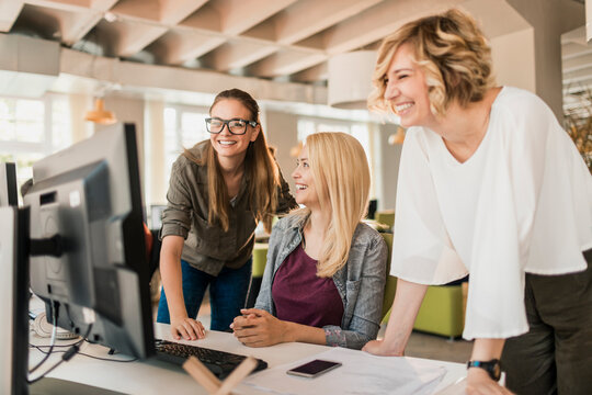 Smiling female coworkers collaborating at computer in modern office