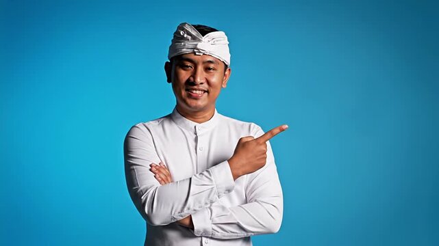 Confident Balinese man in traditional udeng smiling and pointing to an empty digital space, ideal for marketing campaigns, cultural promotions, and engaging advertisements, representing hospitality...