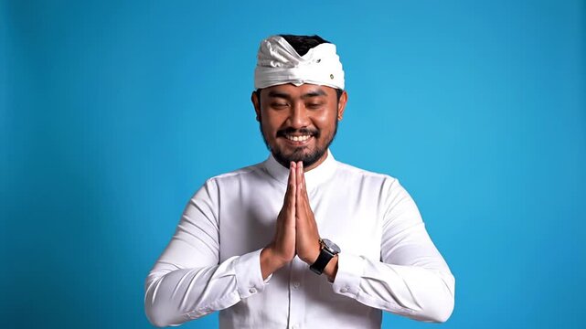 Young Balinese man performing traditional Sembah greeting with folded hands, conveying respect and welcome. Represents Indonesian culture, hospitality, spirituality, and authentic Asian traditions.