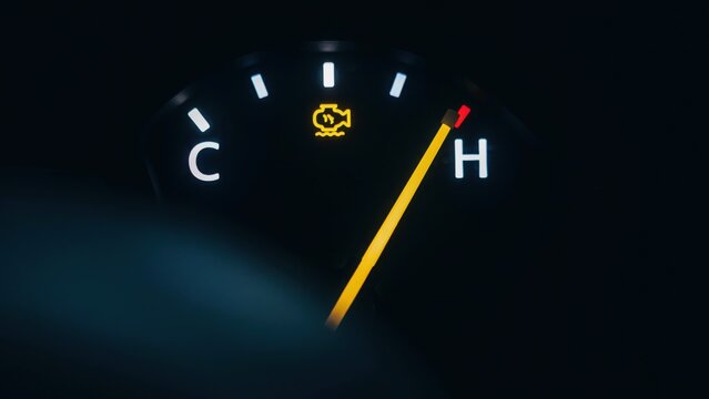 Car dashboard with engine temperature gauge and warning light at night