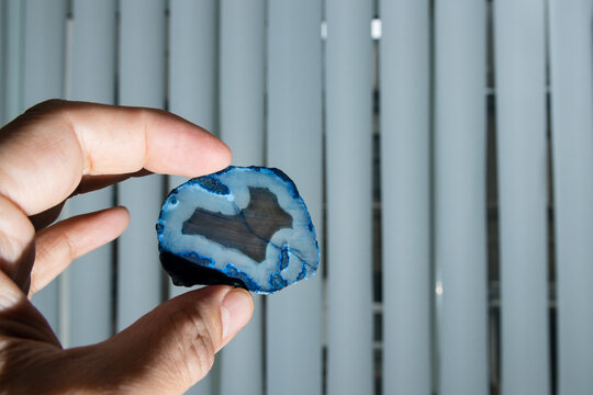 Holding a slice of blue agate stone at a laboratory; on striped background