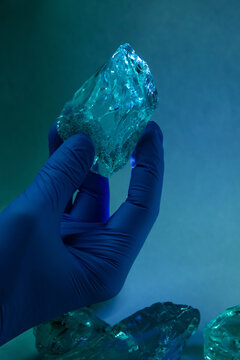 Closeup hand in a rubber glove holding a piece of glass crystal on blurred blue background