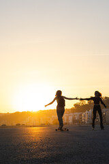 Fototapeta premium Young women collaborating rollerblading and longboarding at sunset
