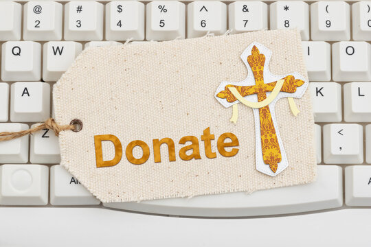 Donate text with a gold cross on a gift tag on white computer keyboard for weekly tithe