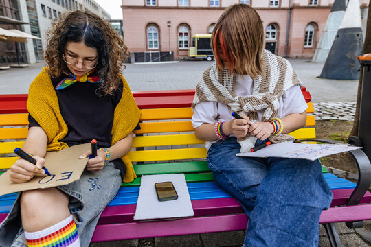 Activists drawing protest signs on a rainbow bench for pride
