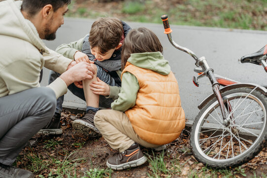 Father comforting son's wound sitting at roadside near bicycle